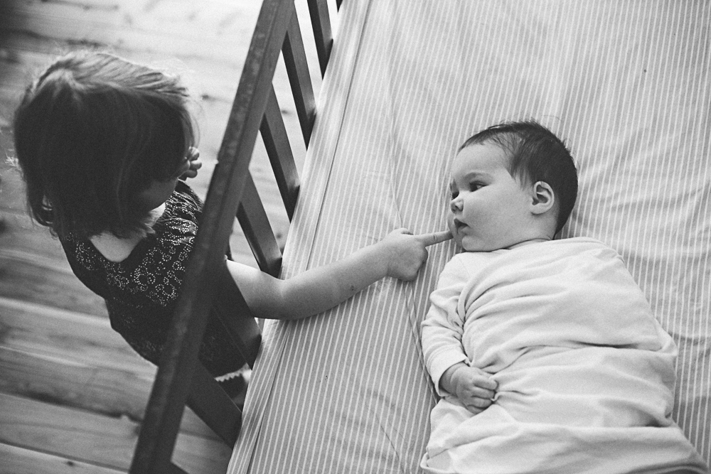 Older sister touching baby's cheek through the cot bars