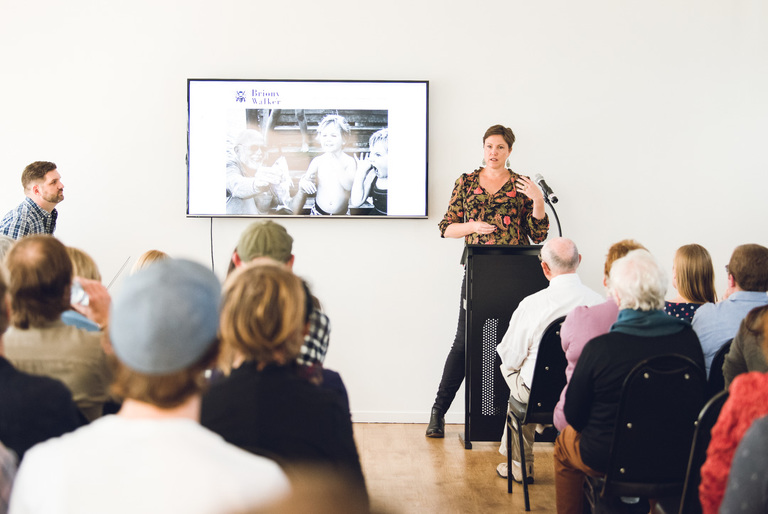 Colour image of Brisbane Photographer Briony Walker presenting a slideshow to a crowded room at CameraPro's Photography Festival