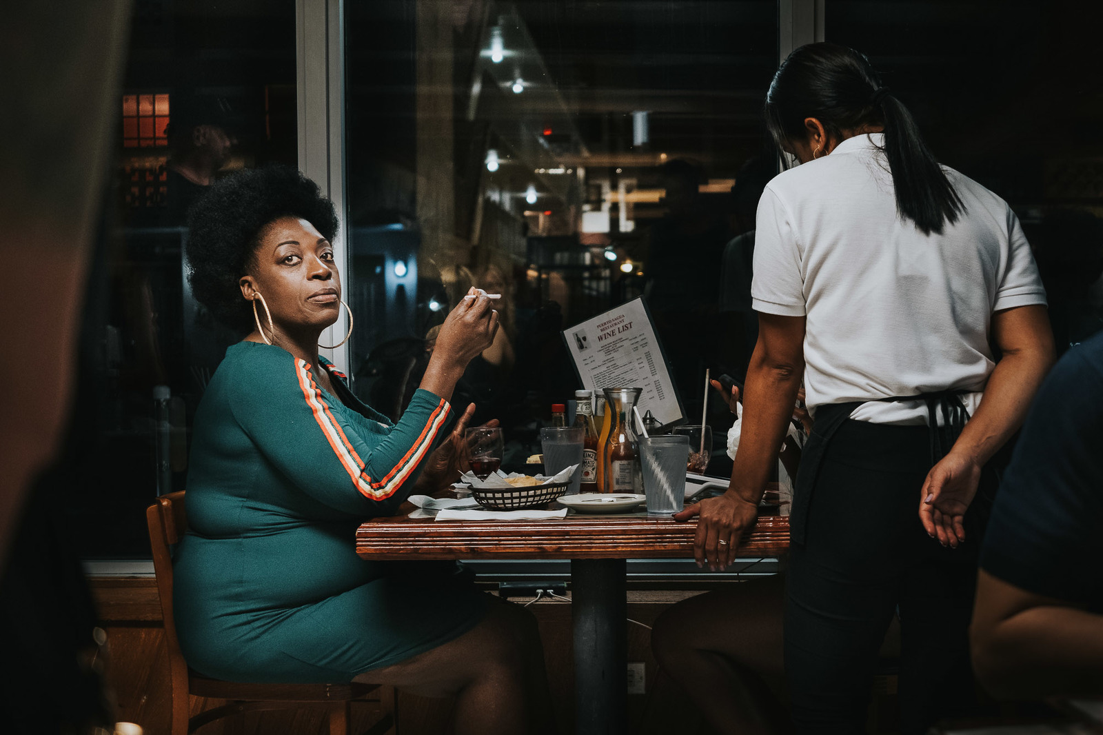 Colour image of an anonymous woman of colour sitting in a cafe in Miami, Florida,looking at the photographer
