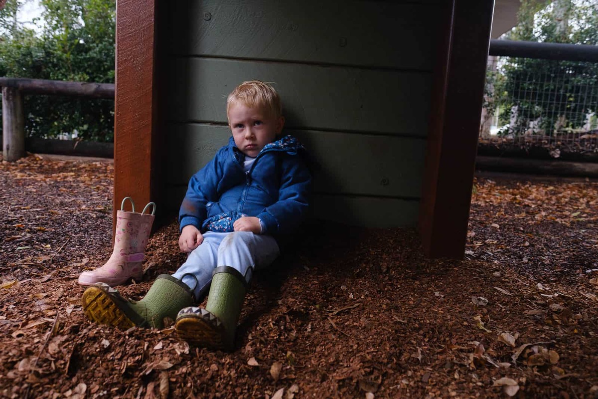 Portrait of a toddler boy dressed in wet weather clothes and boots, with a grumpy face