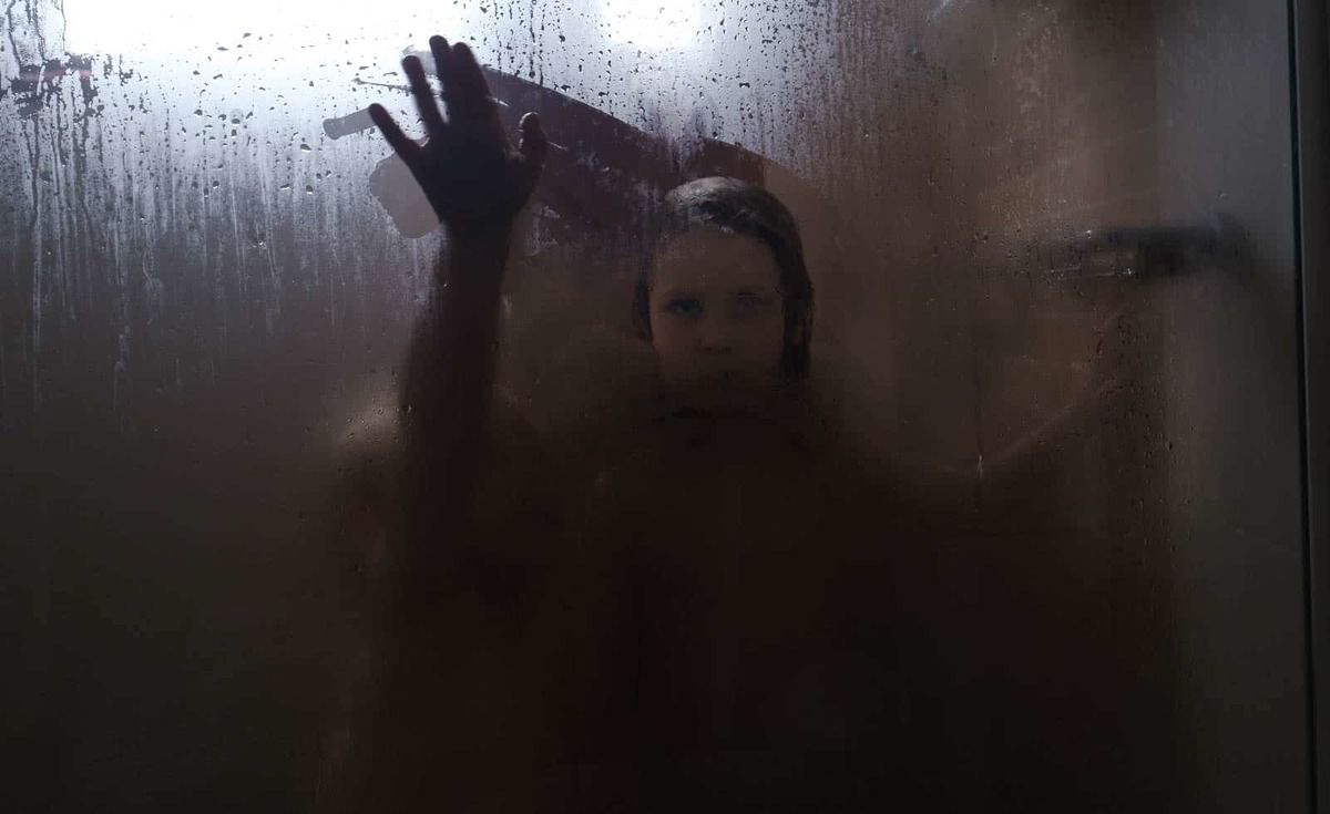 Monochrome image of a child in the shower wiping away the condensation with a hand and an eerie look on her face