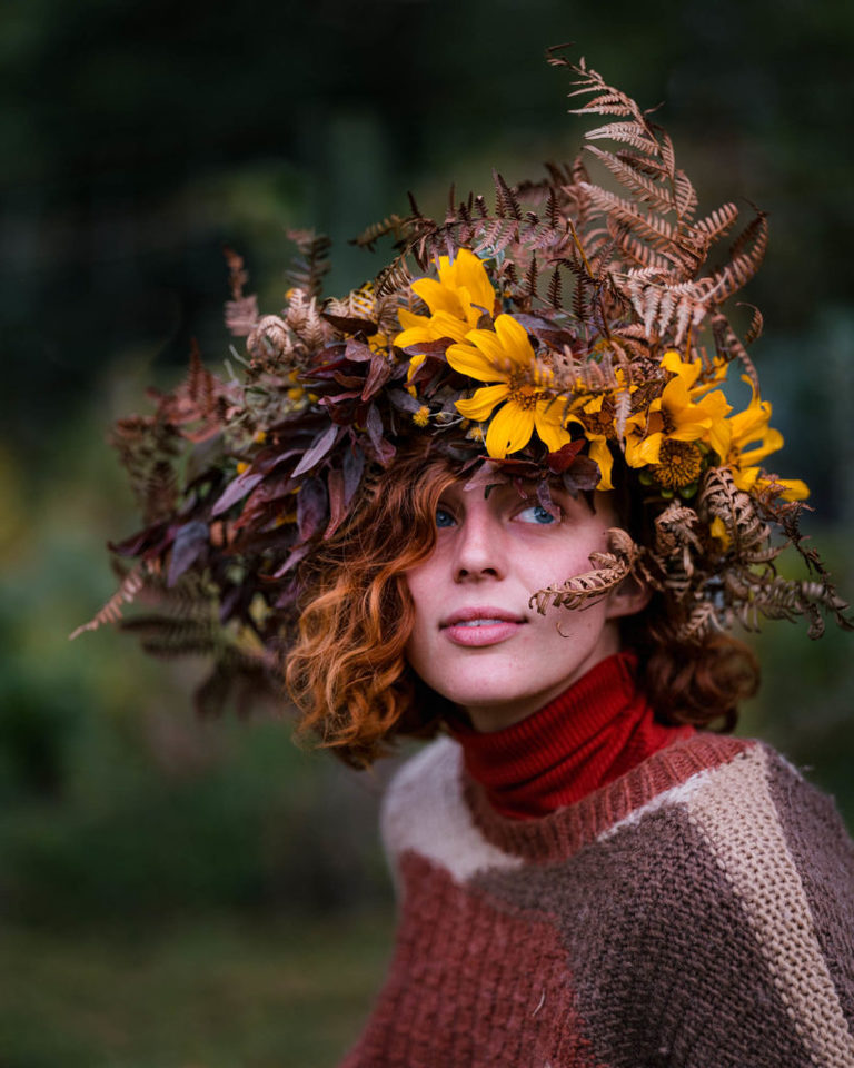 Colour portrait of a woman wearing autumn coloured sweater and a flower and leaf crown. She has vivid blue eyes and striking red hair